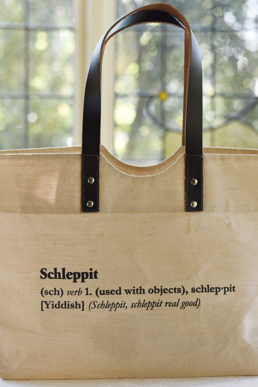 Schlep it, schlep it real good! Need something to schlep your stuff around? This is it. Cooked Concepts' Schleppit (v) Tote is made ethically in India from sustainable Jute, features leather straps and metal rivets and the design is screen printed on the front. 